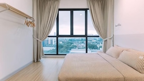 Une chambre avec une grande fenêtre, un lit recouvert d’une couette à carreaux et une vue sur le paysage urbain.