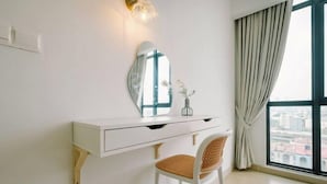 Une coiffeuse blanche avec un miroir, un petit vase avec des fleurs et une chaise en osier.