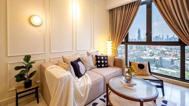 Une chambre d’hôtel moderne, dotée d’un canapé, d’une table ronde, d’une plante en pot et offrant une vue sur la ville grâce à de grandes fenêtres.