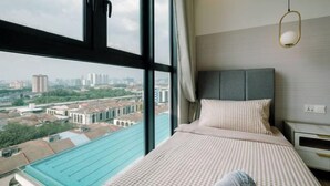 Une chambre d’hôtel dotée d’une grande fenêtre donnant sur la ville, d’un lit avec une literie à carreaux et d’une table de chevet avec une lampe.