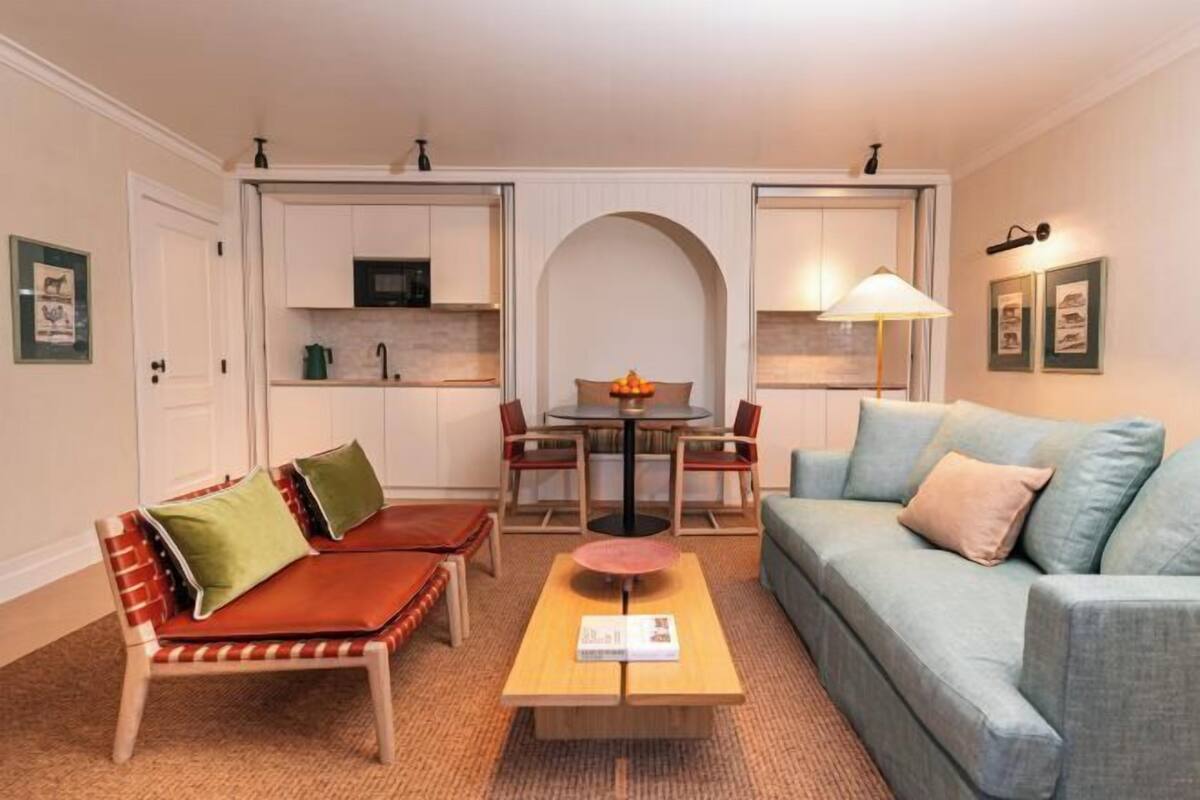 A living room with a sofa, a coffee table, a dining table with chairs, and a kitchen area with cabinets and a microwave.