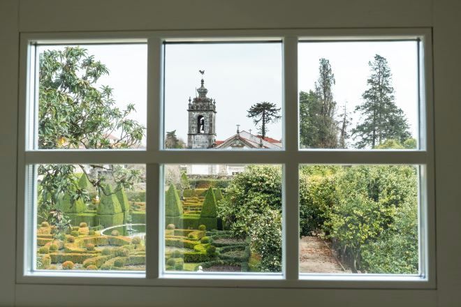 Una finestra de quatre vidres, cada un amb vistes diferents: un arbre, una torre campanar, un bosc dens i un jardí amb formes geomètriques.