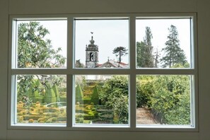 Une fenêtre divisée en quatre panneaux, chacun offrant une vue différente : un arbre, un clocher, une forêt dense et un jardin aux formes géométriques.