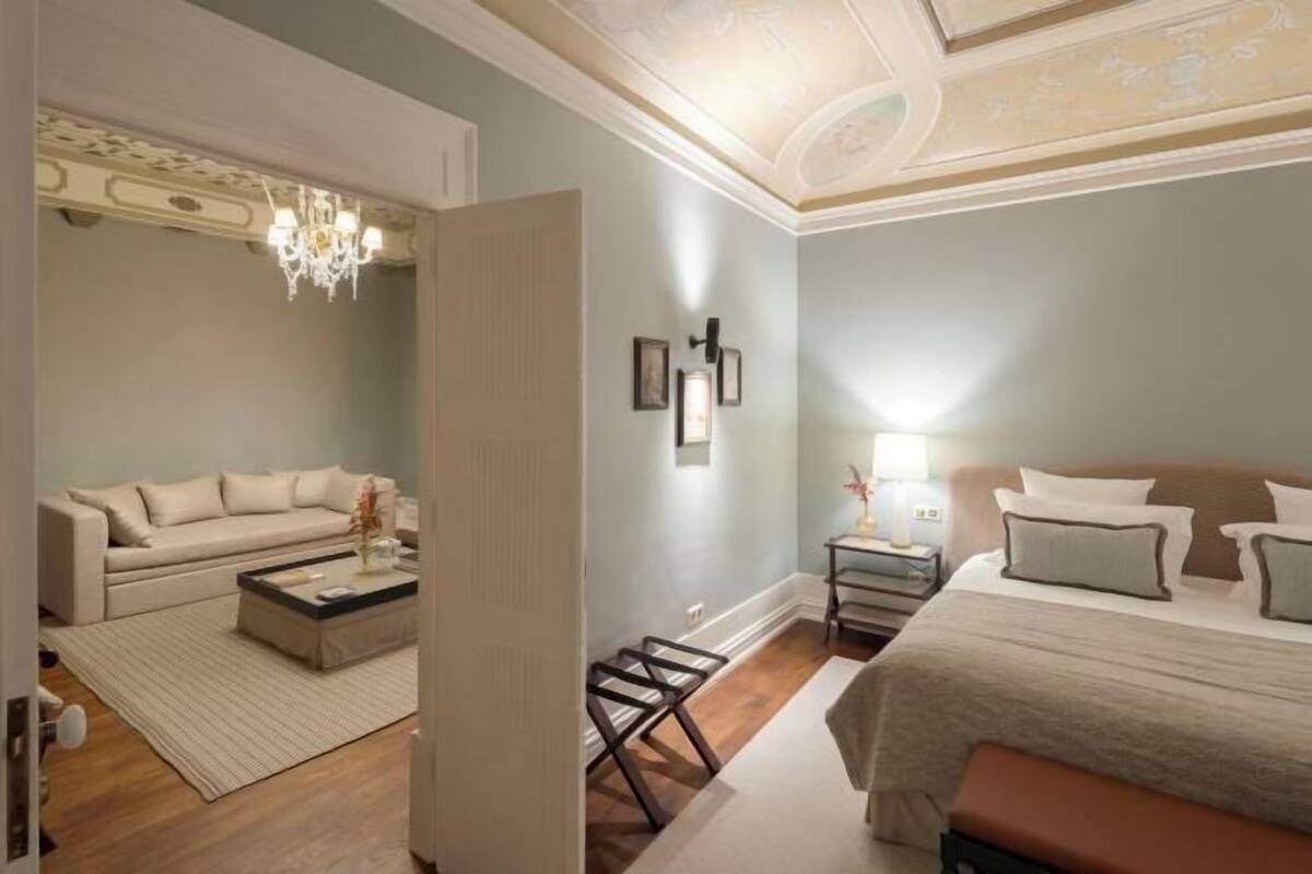 A hotel room with a bed, a sofa, a coffee table, a nightstand, and a chandelier.