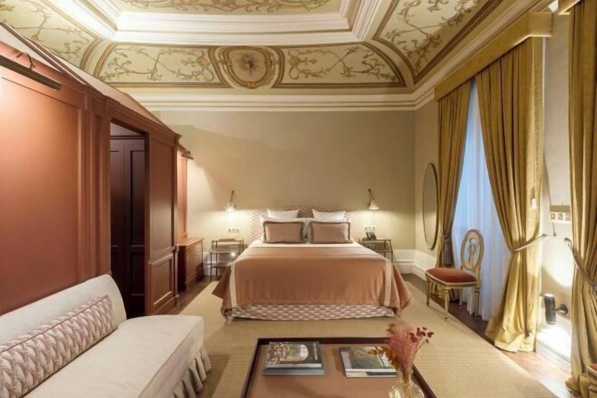 A hotel room with a large bed, a sofa, a coffee table, and a decorative ceiling.