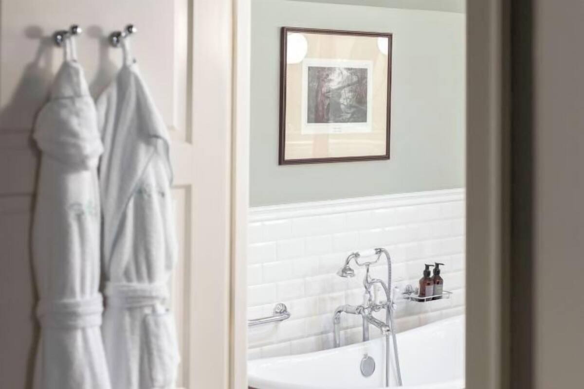 A bathroom with a bathtub, a towel rack with two towels, and a framed picture on the wall.