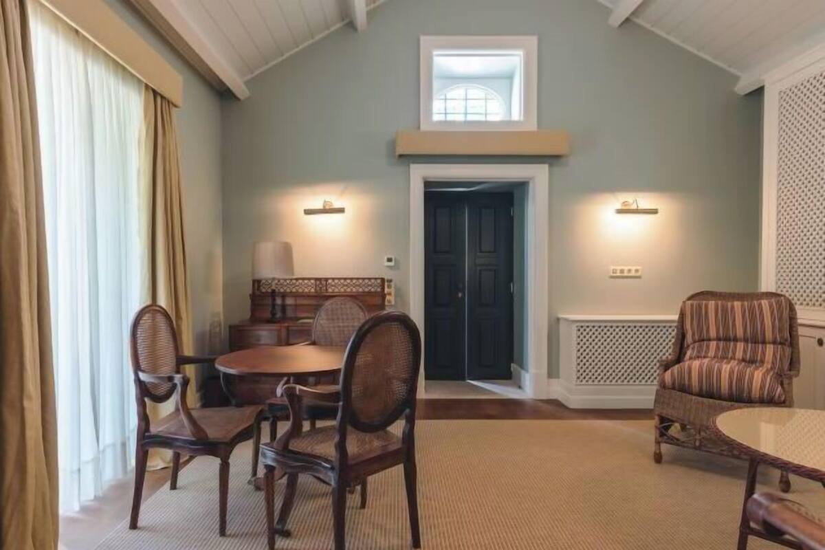 A dining area with a round table and four chairs, a patterned armchair, and a door with a light fixture above it.