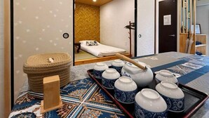 A room with a bed, a bedside table, a wooden stool, and a tray with ceramic cups and a teapot. - Seishukugawa (Osaka)