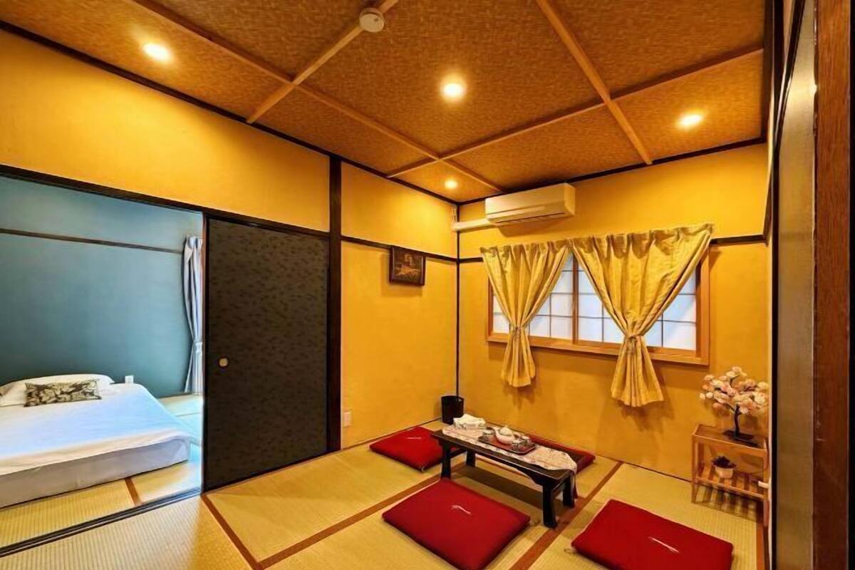 A traditional Japanese-style room with tatami flooring, a bed with a white comforter, a small table with a tea set, and a window with curtains.