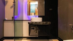 A modern bathroom with a glass shower enclosure, a sink with a marble countertop, and a small trash bin. - Windmill Place Khaoyai (Pak Chong)