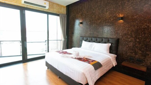 A hotel room with a large bed, a dark headboard, a wooden floor, and a view through a glass door. - Windmill Place Khaoyai (Pak Chong)