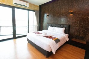 A hotel room with a large bed, a dark headboard, a wooden floor, and a view through a glass door.