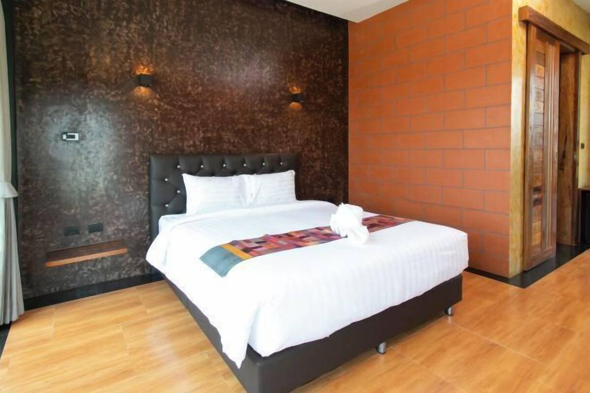 A neatly made bed with a white comforter and pillows, a dark headboard, and a brick accent wall.