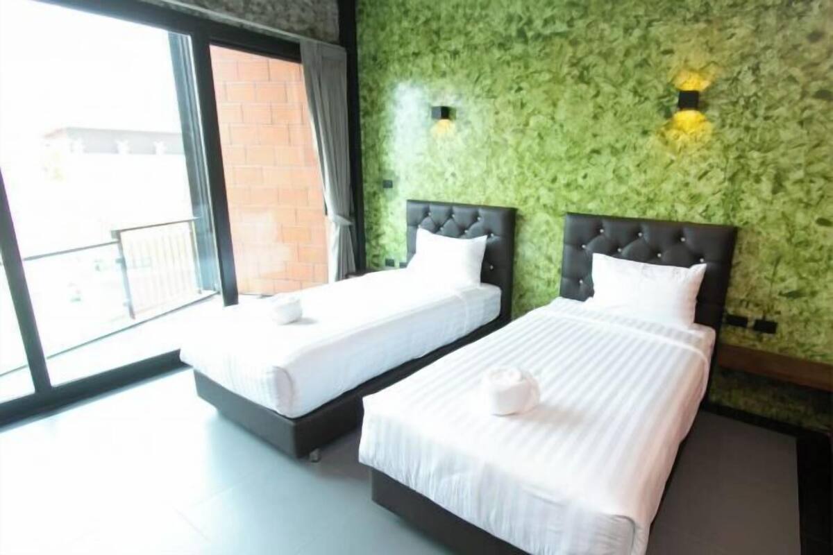 A hotel room with two beds, a green textured wall, and a balcony with a view.