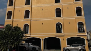 Un edificio de varios pisos con fachada amarilla, varios balcones y una zona de estacionamiento techada.