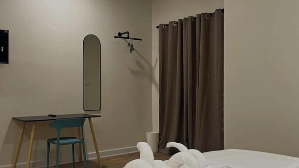 Una habitación de hotel con una cama, un escritorio con silla, un espejo y una cortina.