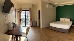 Habitación de hotel con cama, escritorio con silla, televisor montado en la pared y aire acondicionado.