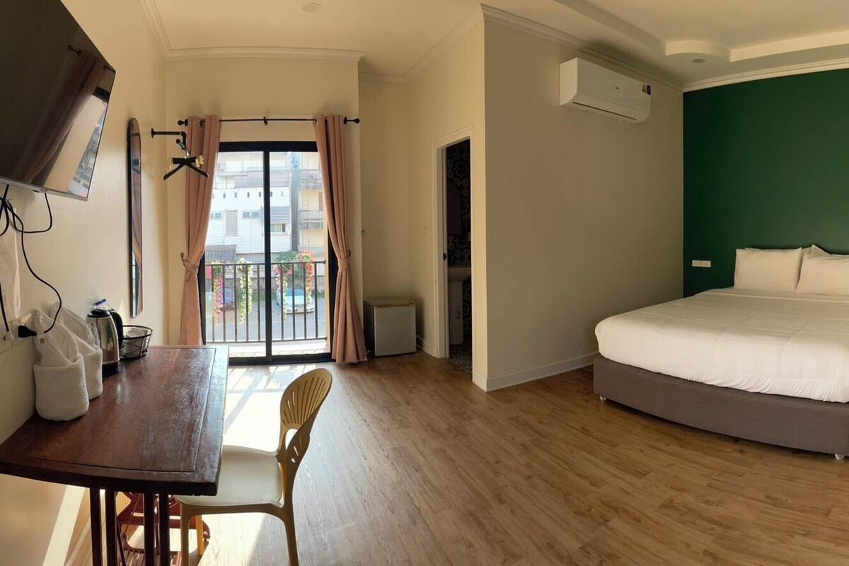 A hotel room with a bed, a desk with a chair, a TV mounted on the wall, and an air conditioning unit.