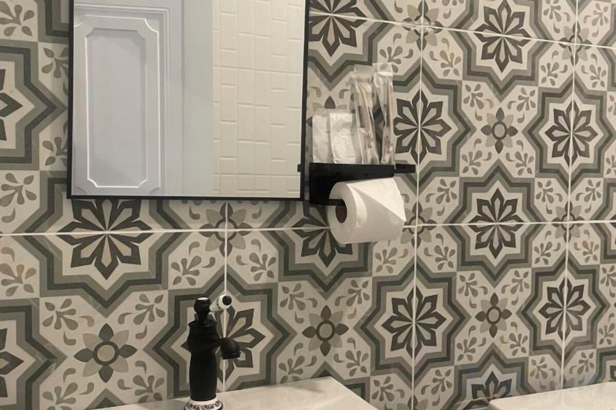 A bathroom with patterned tiles, a toilet paper holder, and a black object on the counter.