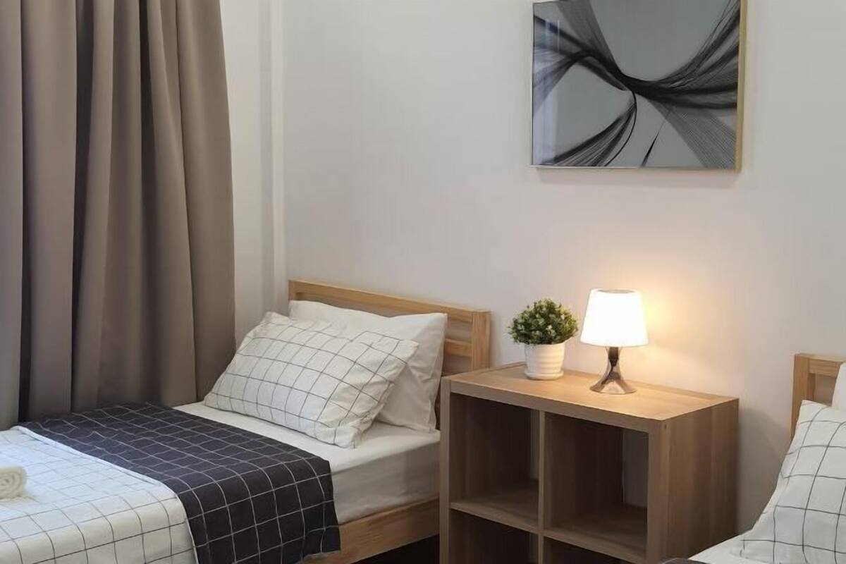 Une chambre d’hôtel avec un lit, une table de chevet avec une lampe, une petite plante et un tableau abstrait accroché au mur.