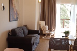 Una sala de estar con un sofá, una silla, una mesa y un ventanal con cortinas.