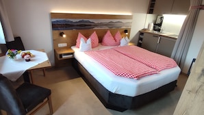 Ett kompakt hotellrum med en säng, ett litet skrivbord med en stol, ett nattduksbord och en TV som är monterad på väggen.