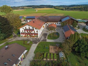 A large, white building with a red roof, surrounded by green fields and a small pond.