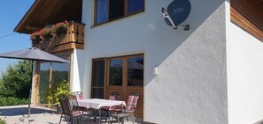 A building with a balcony with flowers, a table with chairs, and a satellite dish.