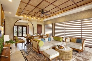 A spacious living area with a ceiling fan, a sofa set, a dining table, and large windows with blinds.