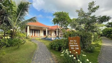 A building with a red roof and a paved pathway leading to it. There is a sign with contact information.