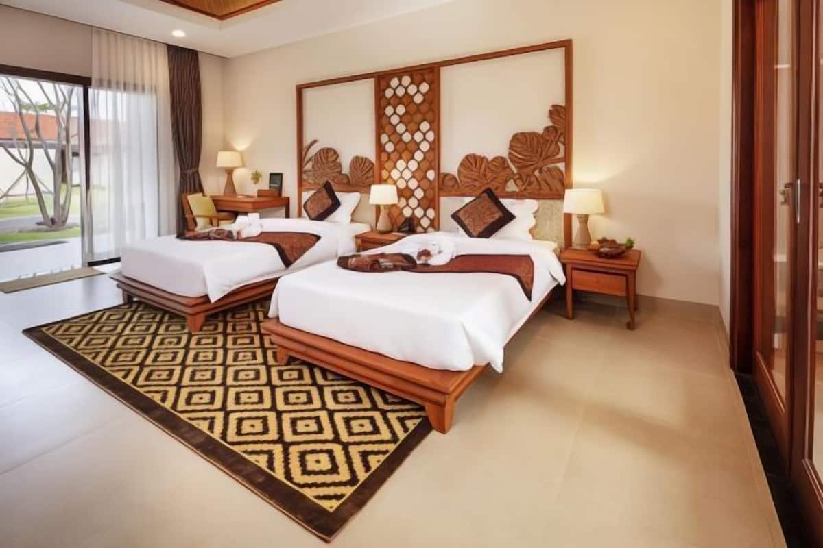 A hotel room with two beds, a large window, a decorative wall, and a patterned rug.