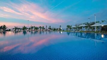 A tranquil infinity pool with a clear view of the horizon, surrounded by palm trees and umbrellas.