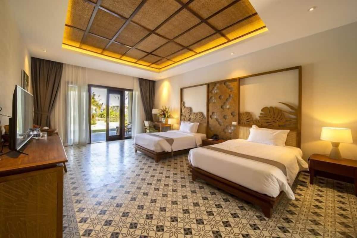 A hotel room with two beds, a desk, a TV, and a large window with curtains.
