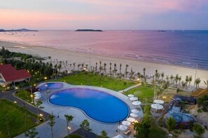 Un resort con una grande piscina, accesso alla spiaggia e palme.