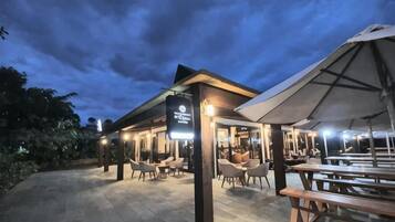An outdoor seating area with tables and chairs, a covered section, and a sign indicating a restaurant or dining area.