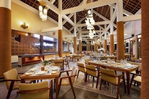A spacious dining area with high ceilings, multiple tables set for dining, and a buffet counter in the background.