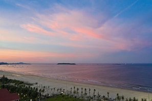 Een uitzicht op het strand met een zonsondergang, palmbomen en een eiland in de verte.