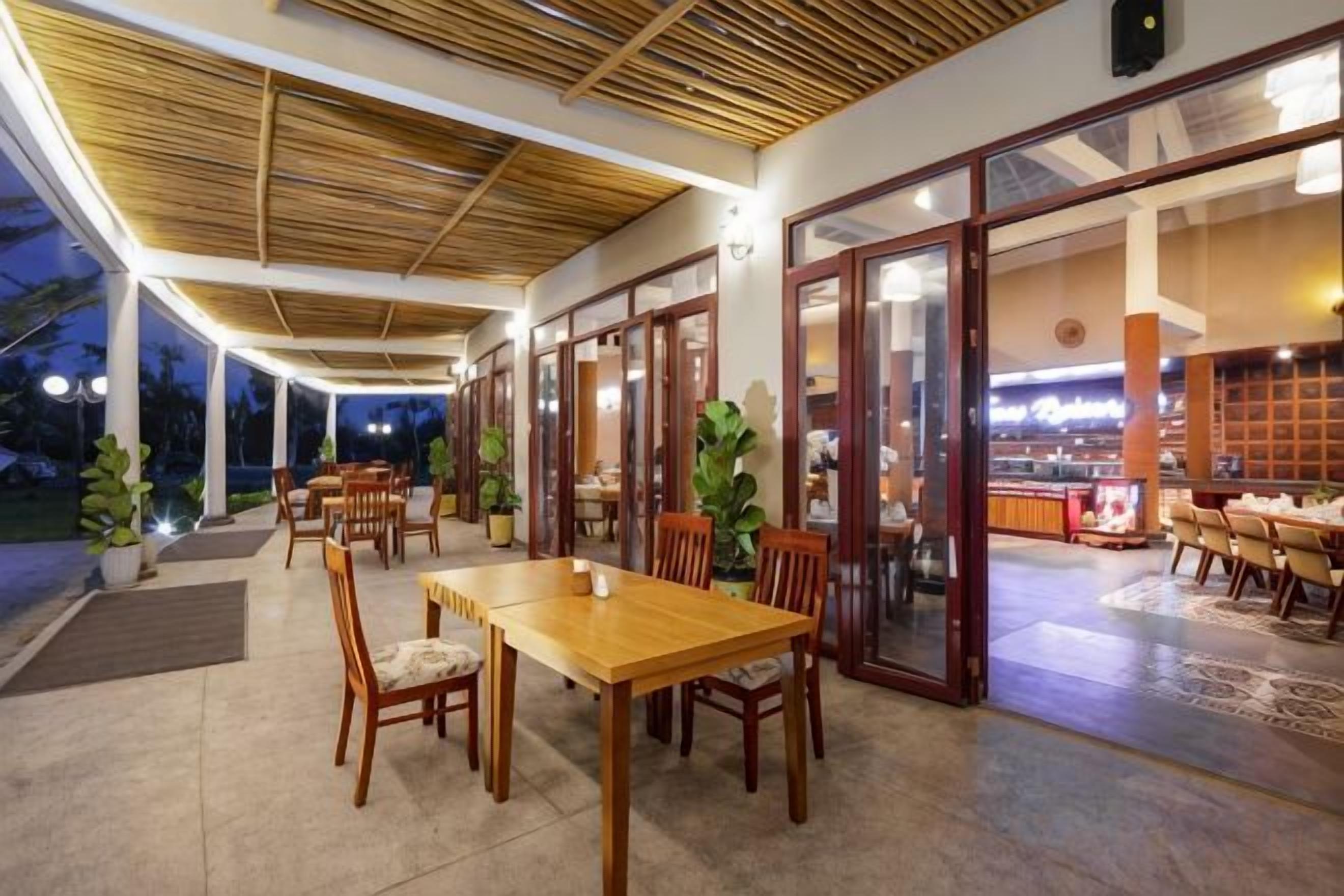 Un área de comedor al aire libre con mesas y sillas, una sección cubierta con techo y vistas al restaurante interior.