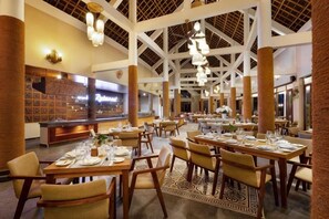 Een ruime eetruimte met meerdere tafels en stoelen, een buffet en een hoog plafond met zichtbare balken.