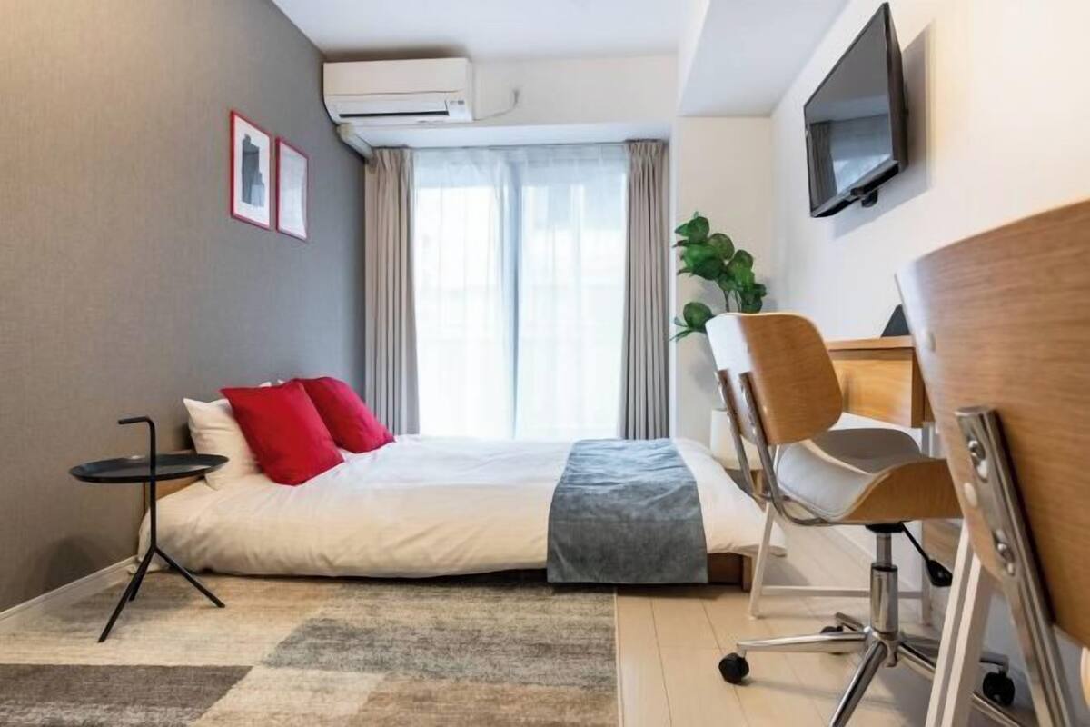 A modern hotel room with a bed, a desk, a chair, a TV, and a window with curtains.