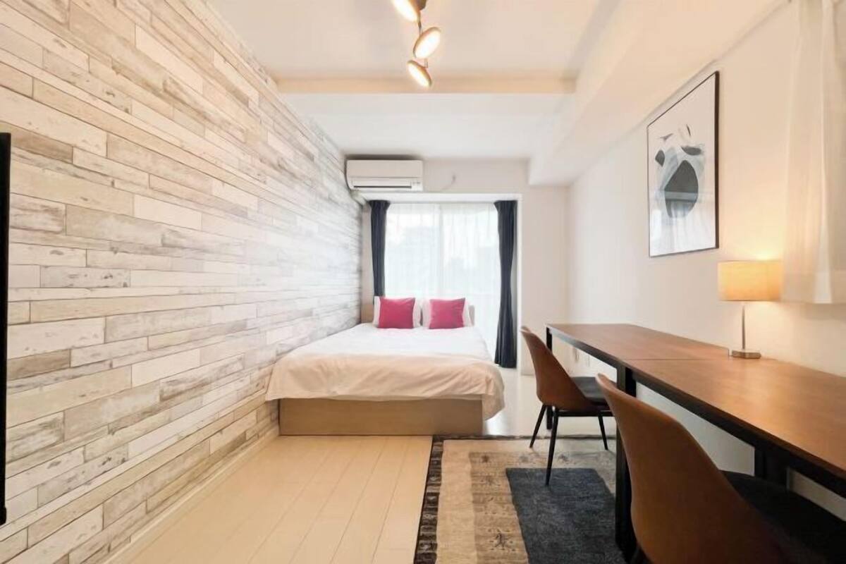 A bedroom with a bed, a desk, a chair, a wall-mounted air conditioner, and a window with curtains.