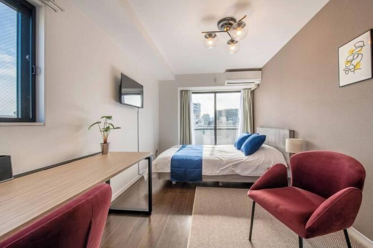 A modern hotel room with a bed, a desk, a chair, a TV, and a city view.