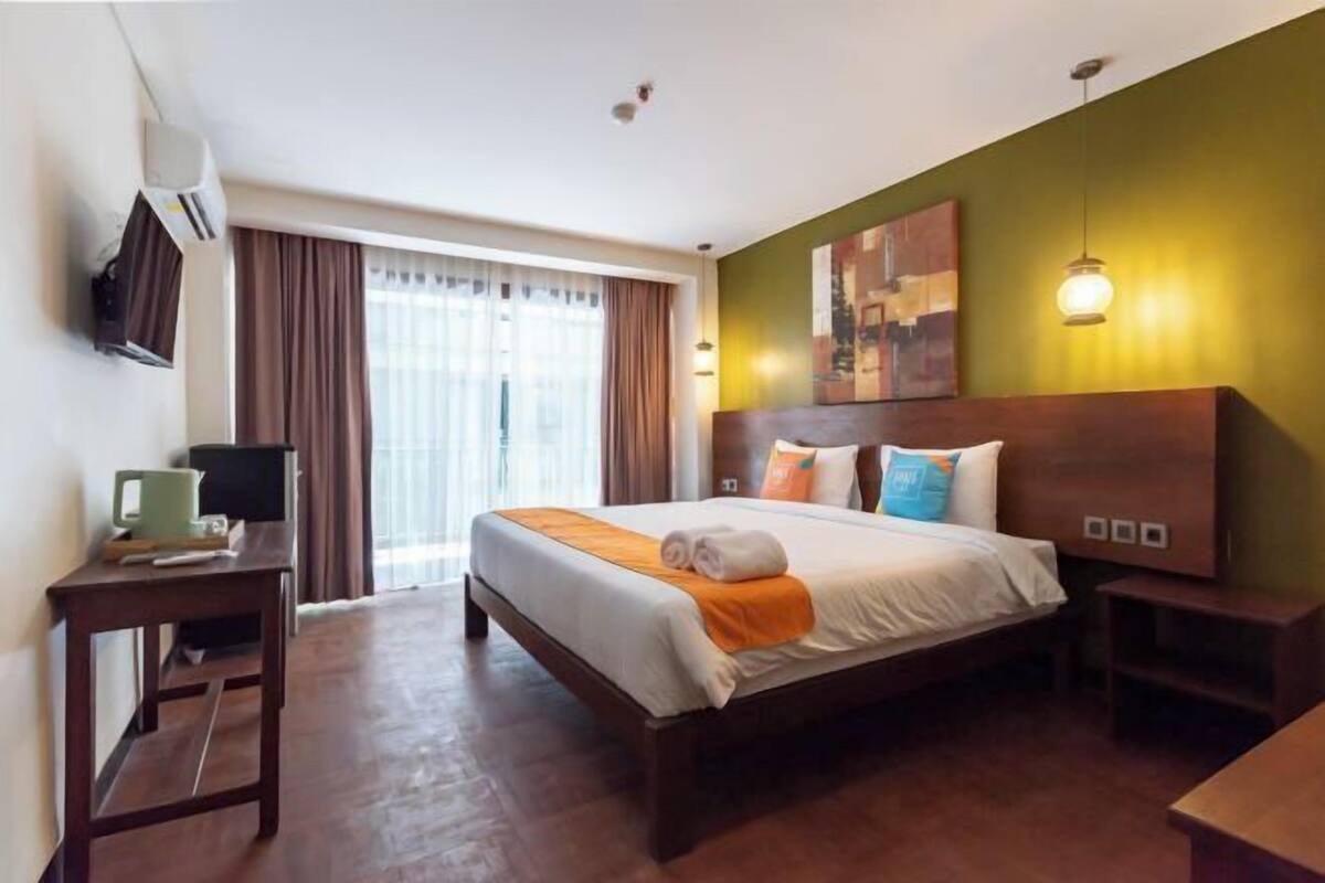 A hotel room with a bed, a desk, a chair, a TV, and a window with curtains.
