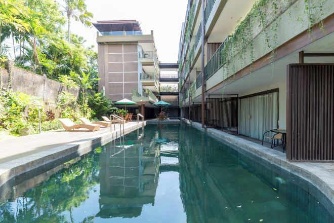 A swimming pool with lounge chairs and umbrellas, surrounded by buildings with balconies and greenery.