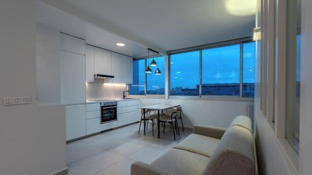 A modern kitchen with white cabinets, a dining area with a table and chairs, and a large window offering a city view. - Apartement Choisy (Paris)