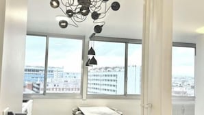 A modern room with large windows, a dining table, and a unique ceiling light fixture. - Apartement Choisy (Paris)