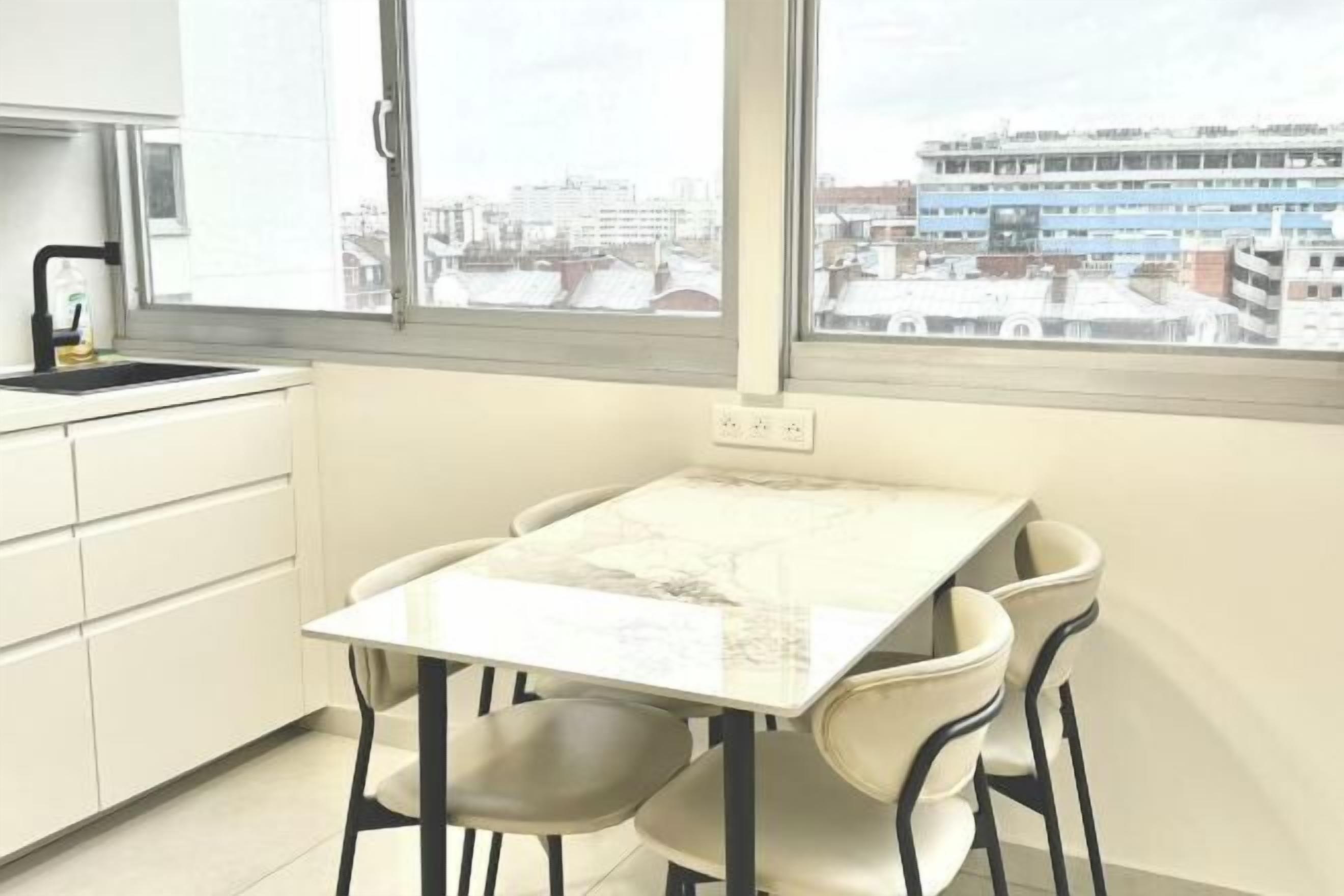 Une cuisine moderne dotée d’un plan de travail en marbre, de meubles blancs et d’une fenêtre donnant sur un paysage urbain.