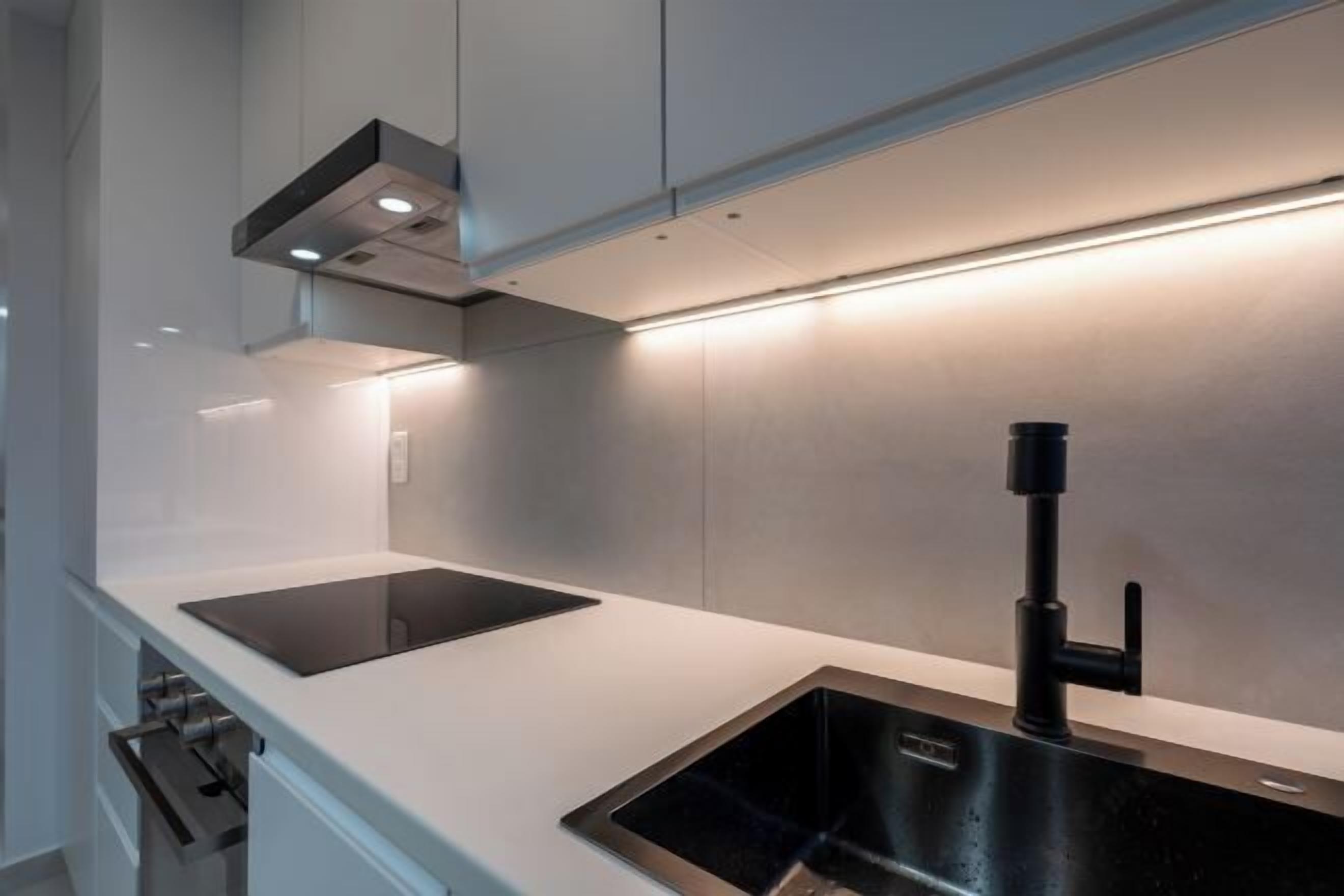 Une cuisine moderne dotée d’un évier noir, d’un plan de travail en acier inoxydable et d’une hotte intégrée.