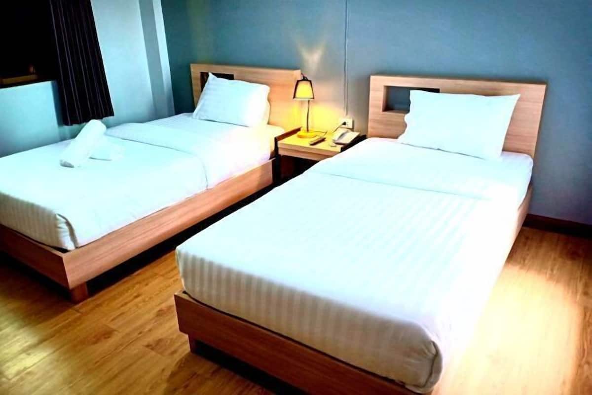 Two single beds with wooden headboards, a nightstand with a lamp, and a window with blinds.
