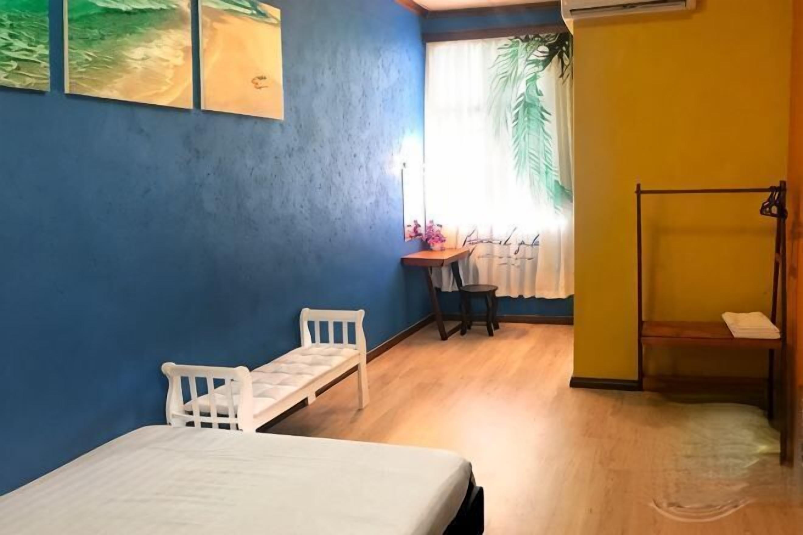 A room with a bed, a desk, a chair, a small table, and a window with curtains.